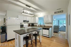 kitchen featuring white cabinets, white appliances, light hardwood / wood-style flooring, decorative light fixtures, and a breakfast bar