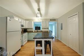 kitchen featuring light hardwood / wood-style floors, a breakfast bar area, white cabinets, a kitchen island, and white appliances