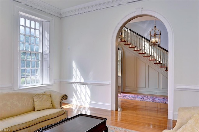 living room featuring wood-type flooring, a notable chandelier, ornamental molding, and a wealth of natural light