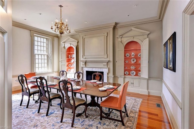 dining area with light hardwood / wood-style flooring, built in shelves, ornamental molding, a chandelier, and a premium fireplace