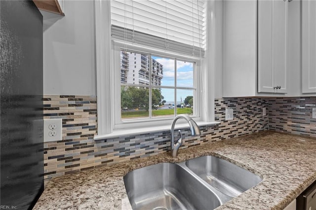 kitchen with black fridge, sink, white cabinets, backsplash, and light stone countertops