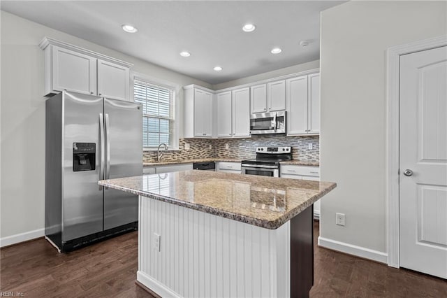 kitchen featuring dark wood-type flooring, light stone counters, white cabinets, stainless steel appliances, and a center island