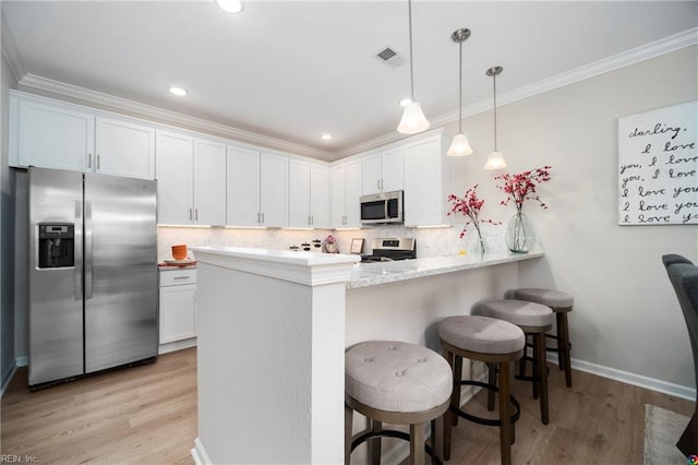 kitchen featuring white cabinets, kitchen peninsula, decorative light fixtures, stainless steel appliances, and a kitchen bar