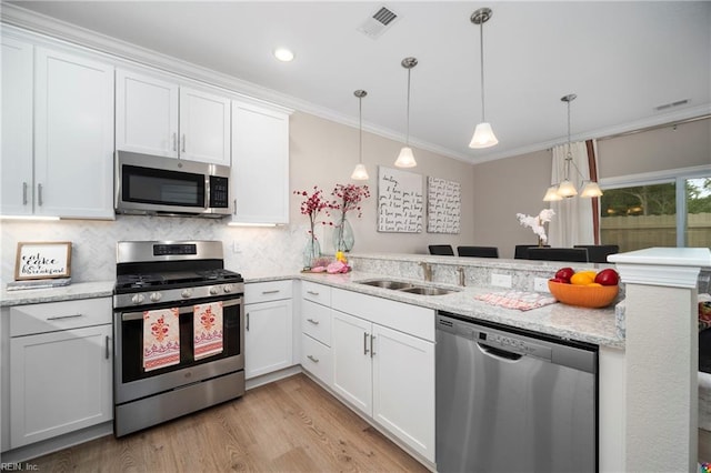 kitchen with pendant lighting, white cabinets, appliances with stainless steel finishes, and crown molding