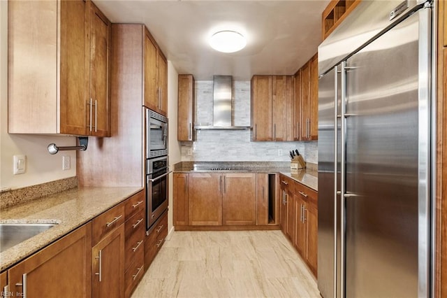 kitchen featuring backsplash, built in appliances, wall chimney range hood, and light stone counters