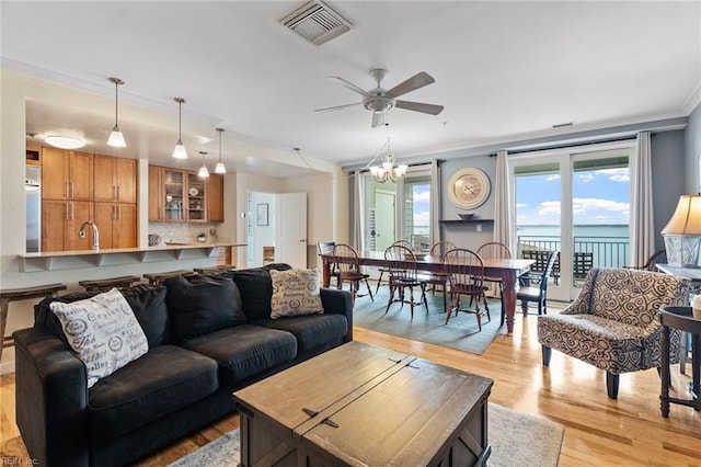 living room with ornamental molding, ceiling fan with notable chandelier, light hardwood / wood-style floors, and a water view