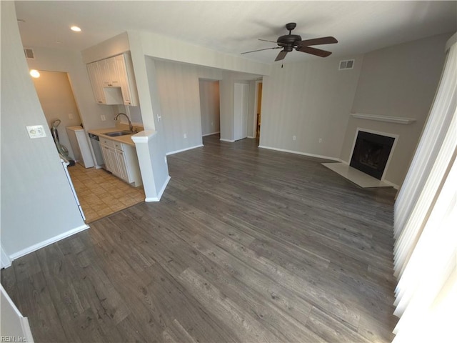 unfurnished living room featuring sink, dark wood-type flooring, a large fireplace, and ceiling fan