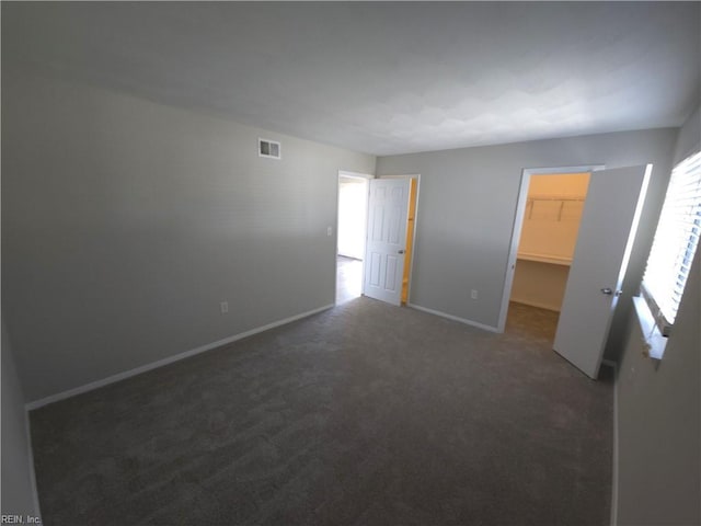 unfurnished bedroom featuring a spacious closet, dark carpet, and a closet