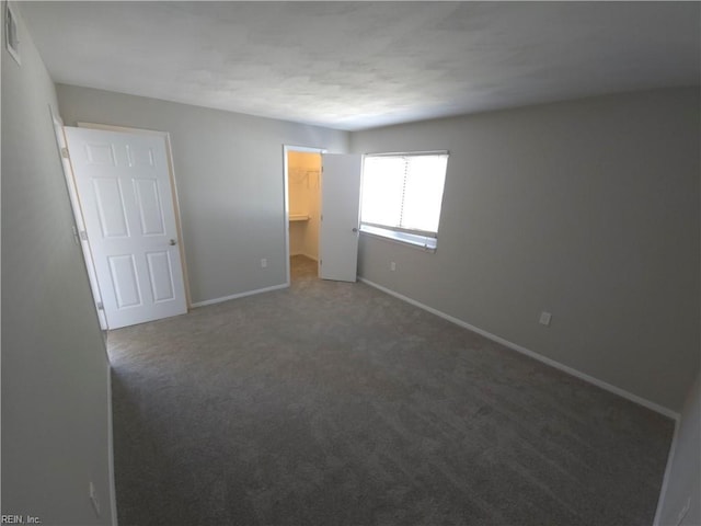 unfurnished bedroom with a walk in closet, dark carpet, and a closet