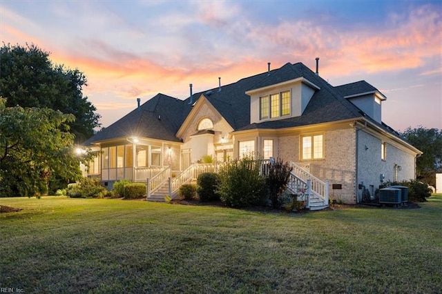 back house at dusk featuring a lawn and central air condition unit