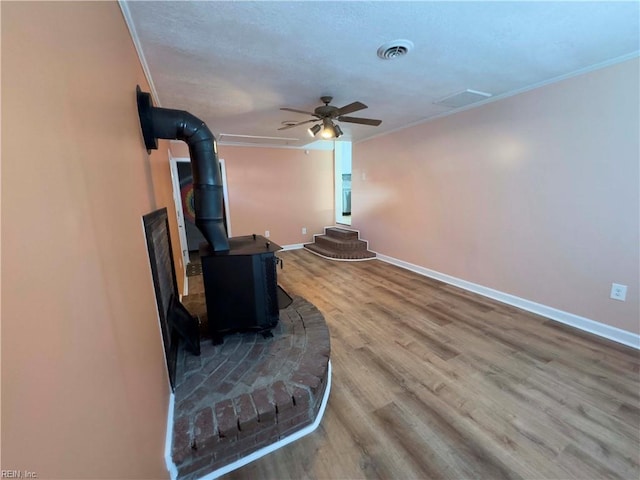 living room with ornamental molding, a wood stove, ceiling fan, and hardwood / wood-style flooring