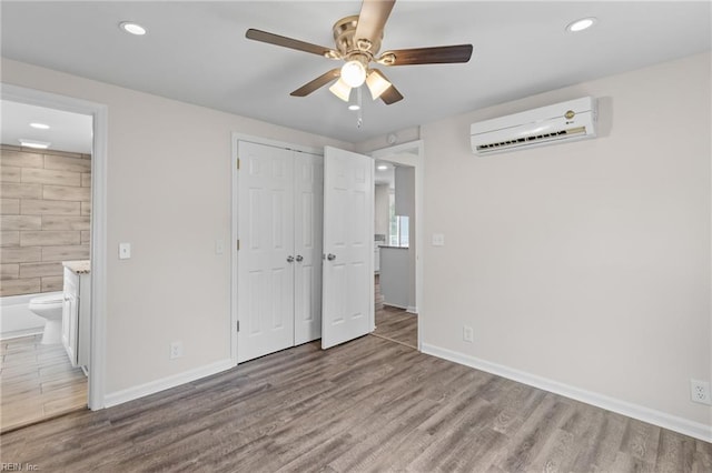 unfurnished bedroom with a closet, light hardwood / wood-style floors, an AC wall unit, ensuite bathroom, and ceiling fan