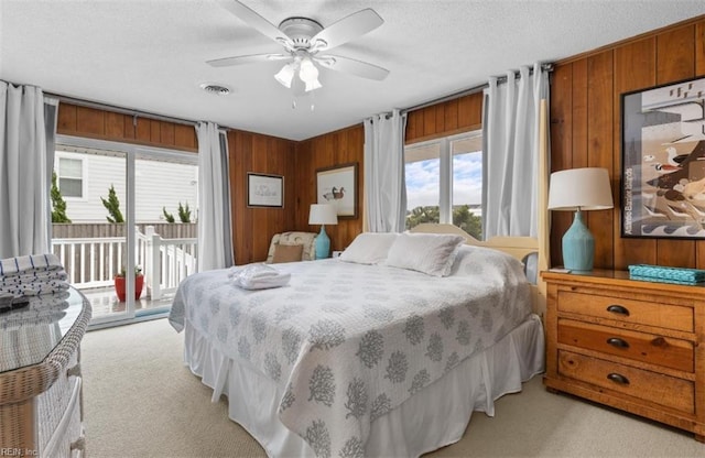 carpeted bedroom with access to outside, a textured ceiling, wood walls, and ceiling fan