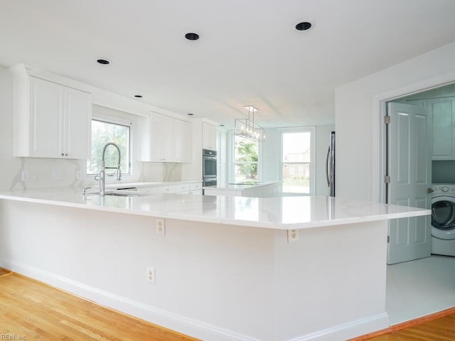 kitchen featuring sink, light wood-type flooring, white cabinetry, and washer / dryer