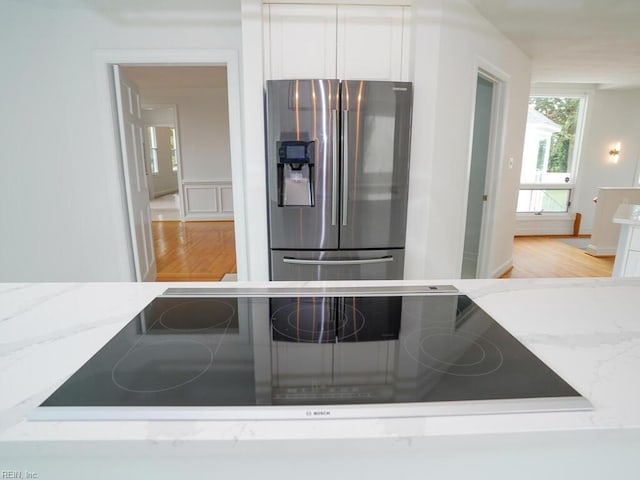 kitchen featuring black electric stovetop, light stone counters, stainless steel refrigerator with ice dispenser, white cabinetry, and hardwood / wood-style floors