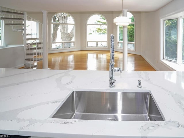 interior details featuring light wood-type flooring, light stone counters, sink, hanging light fixtures, and ornate columns