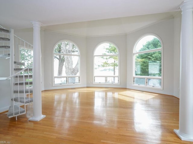 empty room featuring light hardwood / wood-style flooring, ornamental molding, and ornate columns