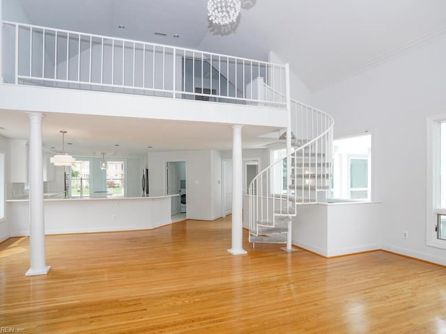 unfurnished living room featuring high vaulted ceiling, an inviting chandelier, hardwood / wood-style floors, and ornate columns