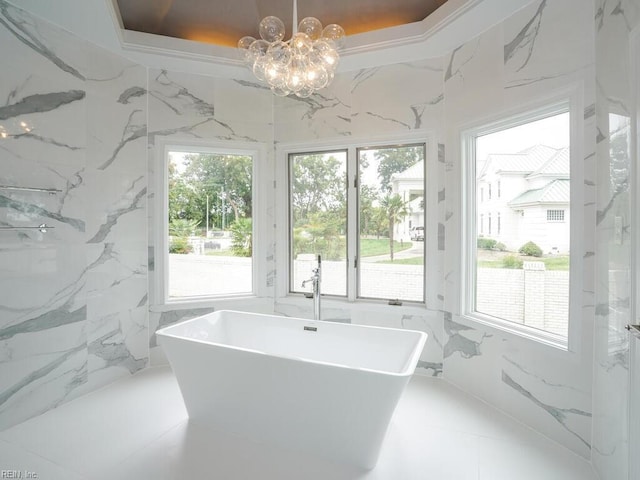 bathroom with an inviting chandelier, a raised ceiling, plenty of natural light, and a washtub