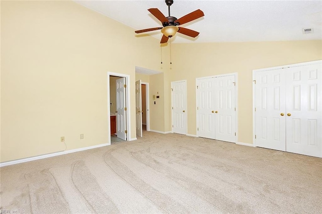 unfurnished bedroom with ceiling fan, high vaulted ceiling, two closets, light carpet, and ensuite bathroom