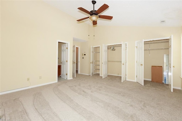 unfurnished bedroom with ceiling fan, multiple closets, light carpet, and high vaulted ceiling