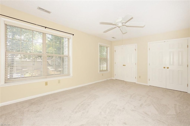 unfurnished bedroom featuring light carpet, ceiling fan, and multiple closets