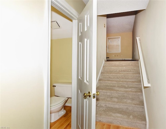 staircase with a textured ceiling and wood-type flooring