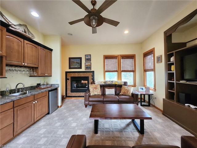 kitchen with a fireplace, ceiling fan, stainless steel dishwasher, sink, and light colored carpet