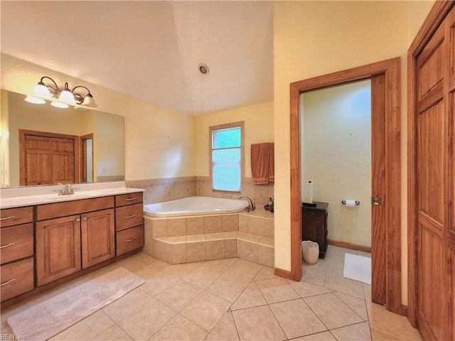 bathroom featuring tiled tub, vanity, vaulted ceiling, and tile patterned floors