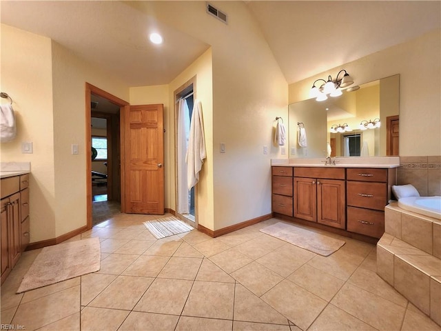 bathroom with tiled tub, vanity, tile patterned flooring, and vaulted ceiling