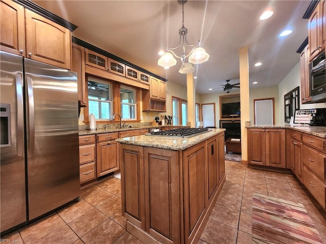 kitchen with appliances with stainless steel finishes, ceiling fan with notable chandelier, a kitchen island, pendant lighting, and tile patterned flooring