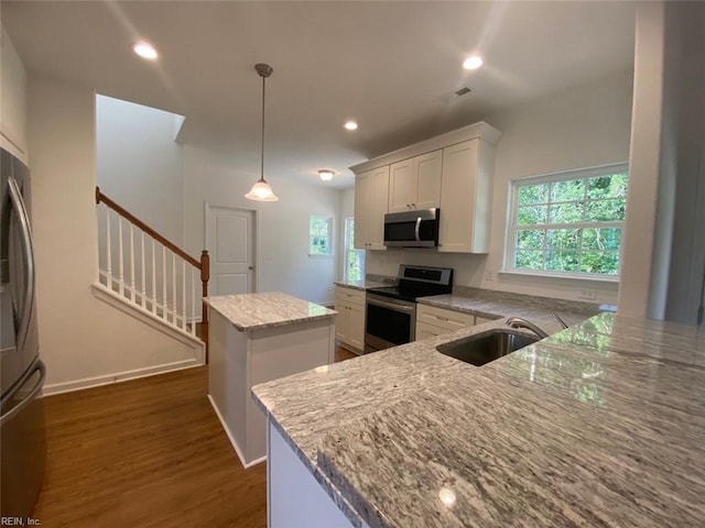 kitchen featuring light stone counters, white cabinets, stainless steel appliances, a center island, and sink