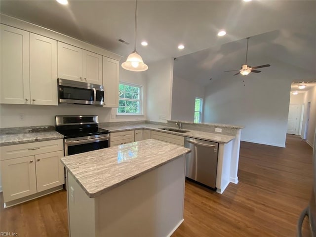 kitchen featuring appliances with stainless steel finishes, hanging light fixtures, dark wood-type flooring, white cabinets, and a kitchen island