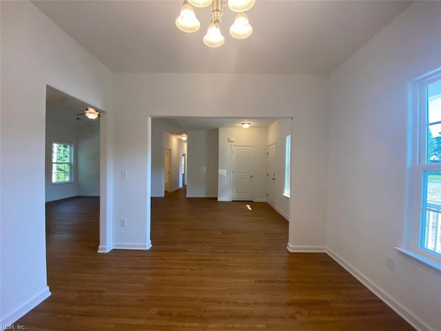 unfurnished room with ceiling fan with notable chandelier, dark wood-type flooring, and a healthy amount of sunlight