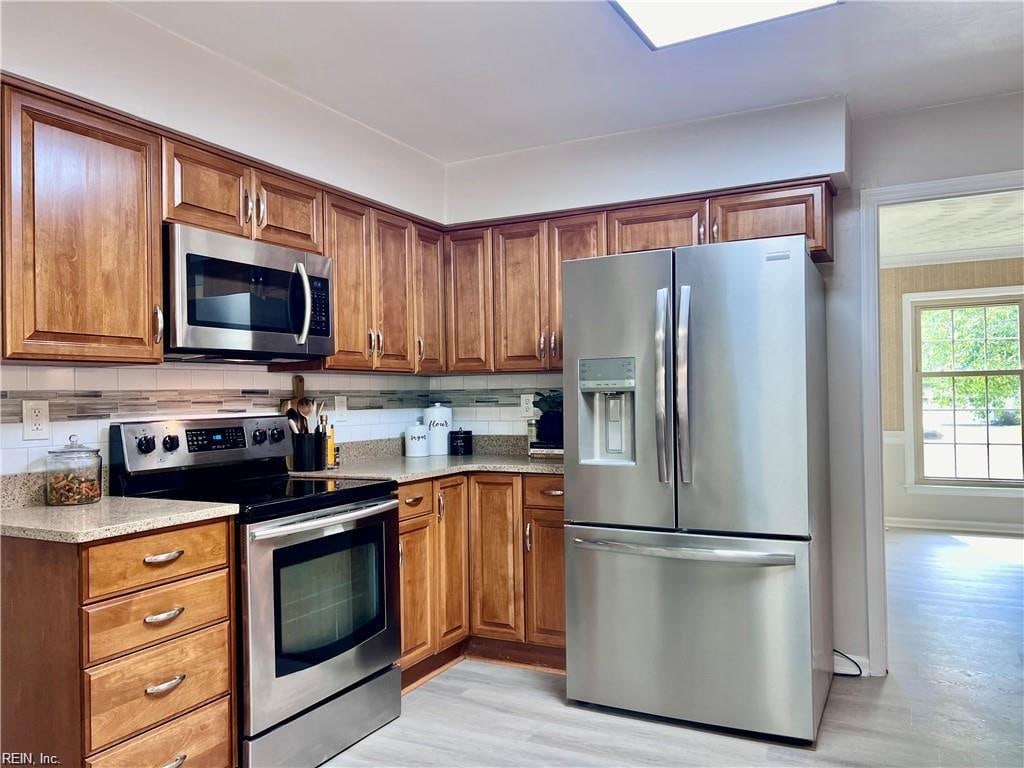 kitchen featuring light stone countertops, appliances with stainless steel finishes, light hardwood / wood-style floors, and decorative backsplash