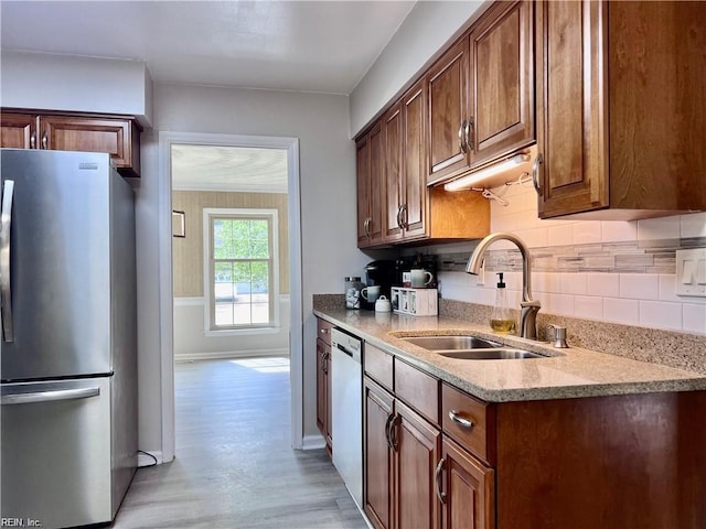 kitchen with appliances with stainless steel finishes, decorative backsplash, light wood-type flooring, and sink