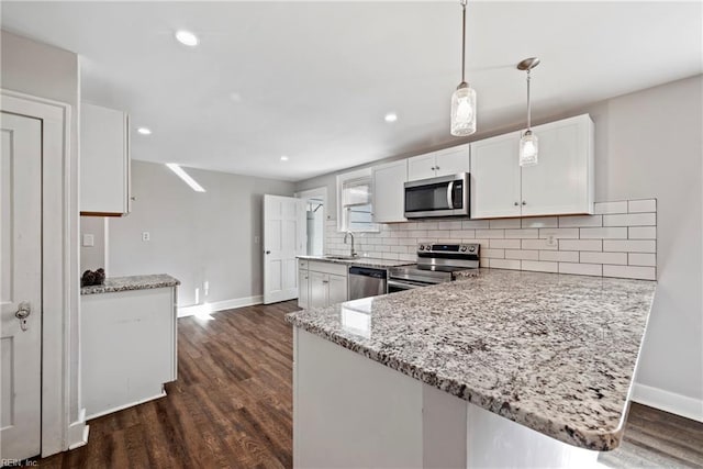 kitchen featuring pendant lighting, white cabinets, kitchen peninsula, appliances with stainless steel finishes, and dark hardwood / wood-style flooring