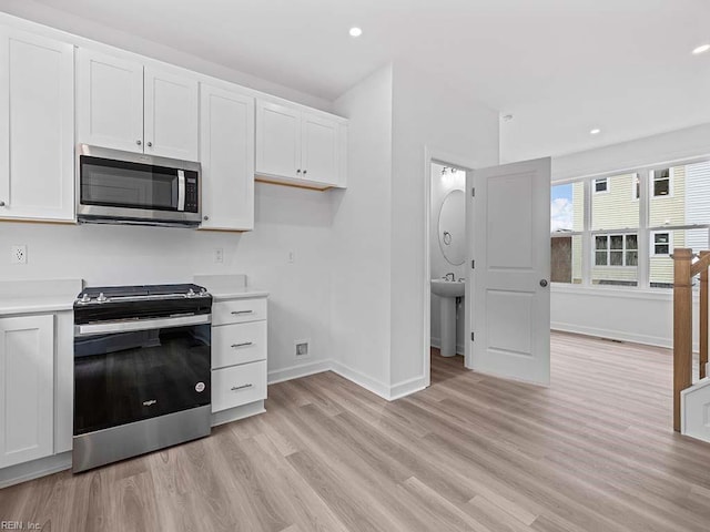 kitchen with stainless steel appliances, white cabinets, and light hardwood / wood-style floors