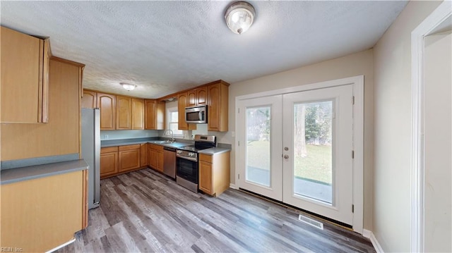 kitchen with a textured ceiling, sink, light hardwood / wood-style flooring, appliances with stainless steel finishes, and french doors