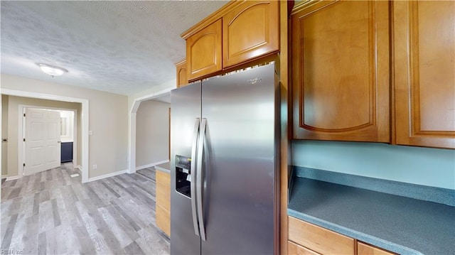 kitchen featuring light wood-type flooring, stainless steel refrigerator with ice dispenser, and a textured ceiling