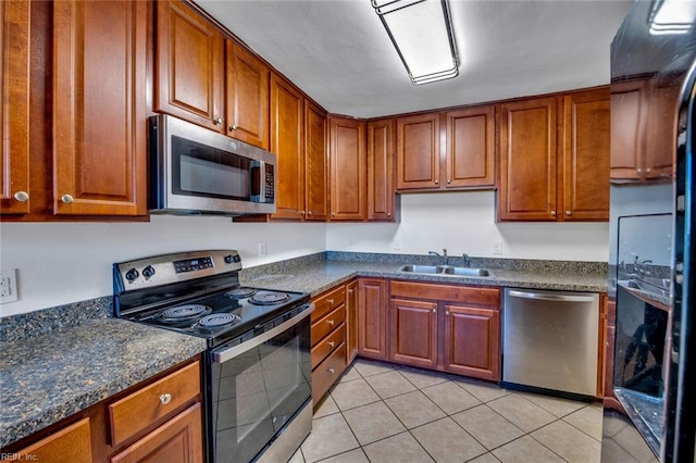 kitchen with dark stone countertops, sink, light tile patterned floors, and stainless steel appliances