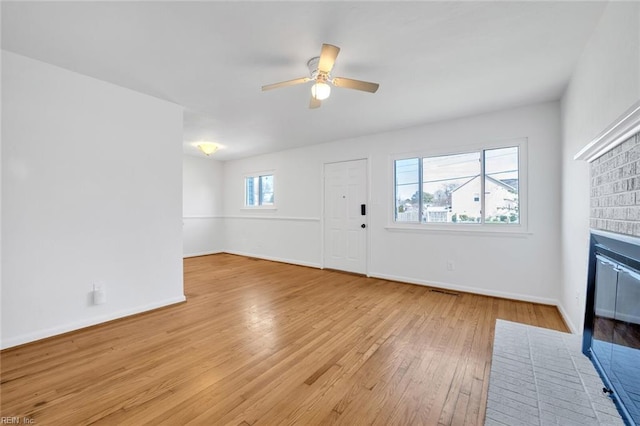 entryway with a healthy amount of sunlight, light hardwood / wood-style floors, ceiling fan, and a brick fireplace