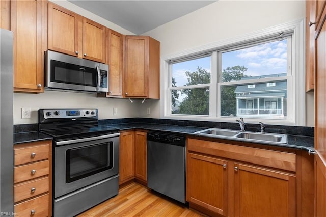 kitchen featuring light wood-type flooring, dark stone countertops, appliances with stainless steel finishes, and sink