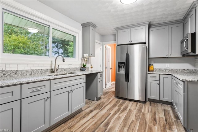 kitchen with light hardwood / wood-style flooring, appliances with stainless steel finishes, light stone countertops, and sink