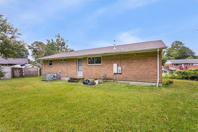 rear view of property with central AC unit and a yard