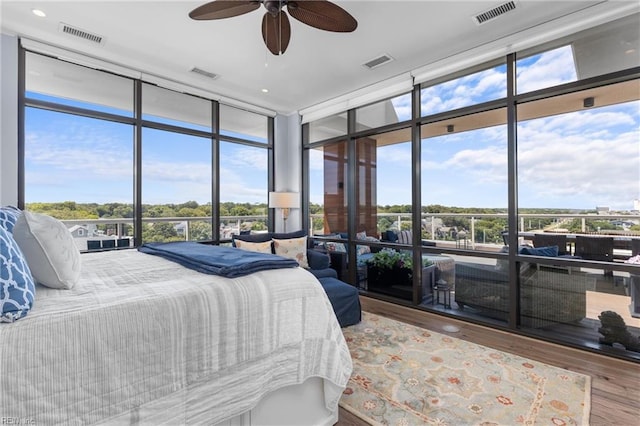 bedroom featuring multiple windows, hardwood / wood-style floors, expansive windows, and ceiling fan