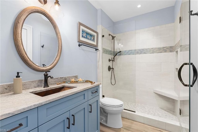 bathroom with hardwood / wood-style floors, walk in shower, vanity, and toilet