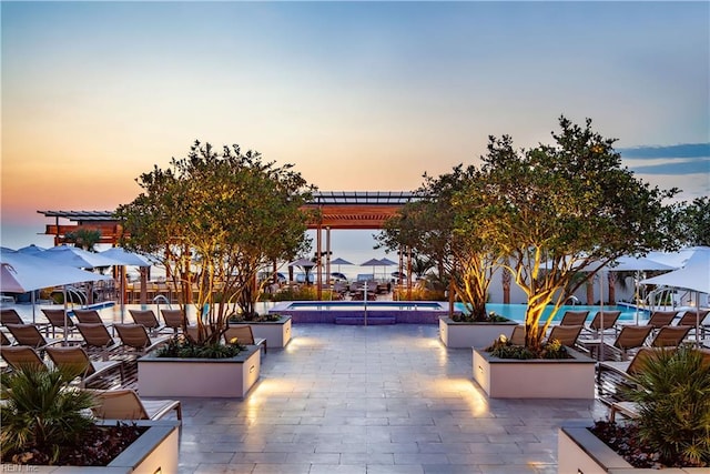 patio terrace at dusk featuring a community pool