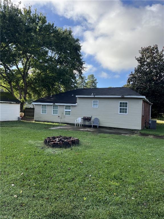 back of property with a fire pit and a lawn