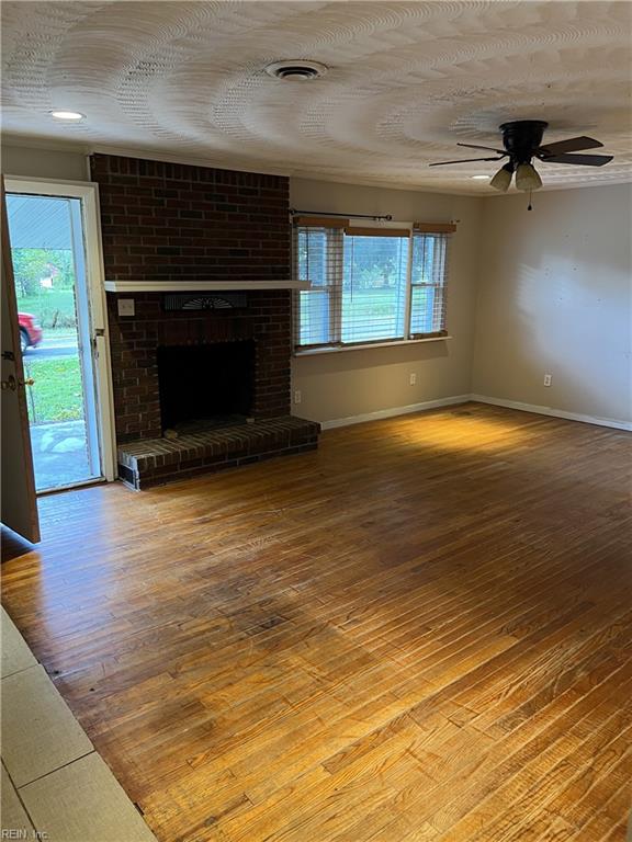 unfurnished living room with a healthy amount of sunlight, a brick fireplace, ceiling fan, and hardwood / wood-style floors